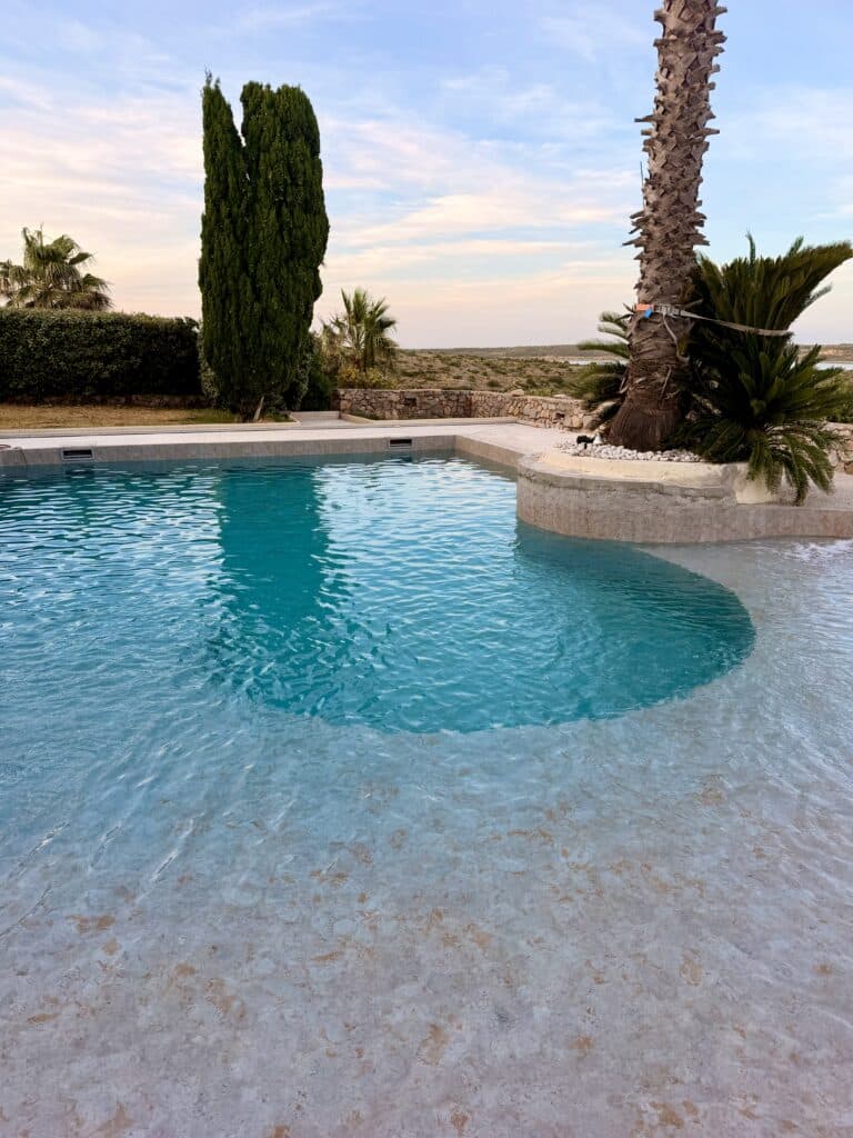 Piscine Extérieure avec Palmier et Vue Panoramique Piscine turquoise avec palmier et cyprès au crépuscule sur un paysage vallonné.