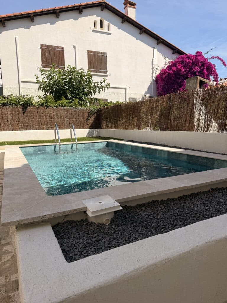 Piscine moderne rectangulaire, jardin avec maison blanche et bougainvillier rose.