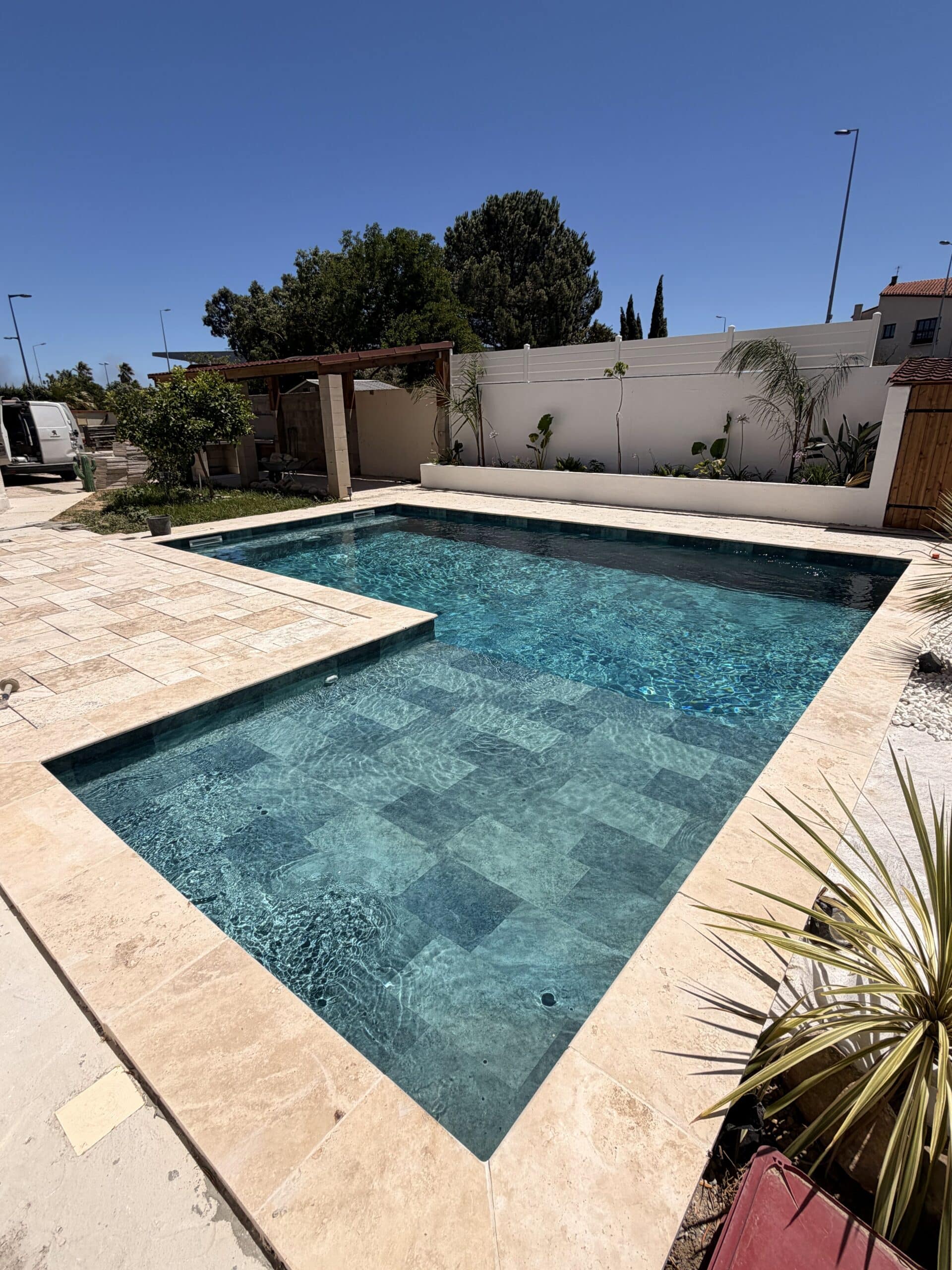 Piscine moderne à plage immergée avec terrasse en travertin et jardin paysager.