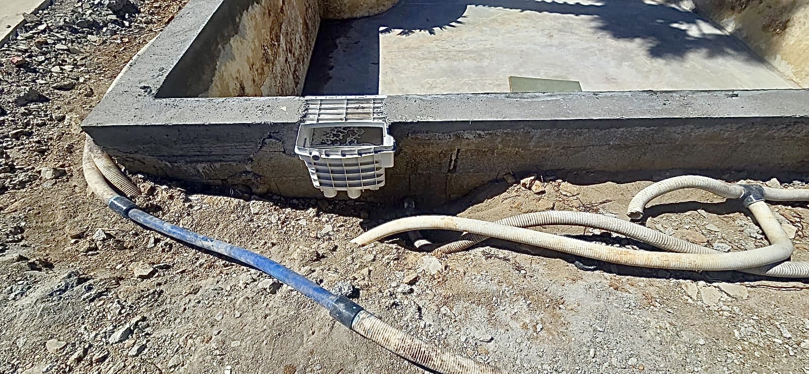 Skimmer de piscine encastré dans une paroi en béton sur un chantier de construction avec des tuyaux flexibles au sol.