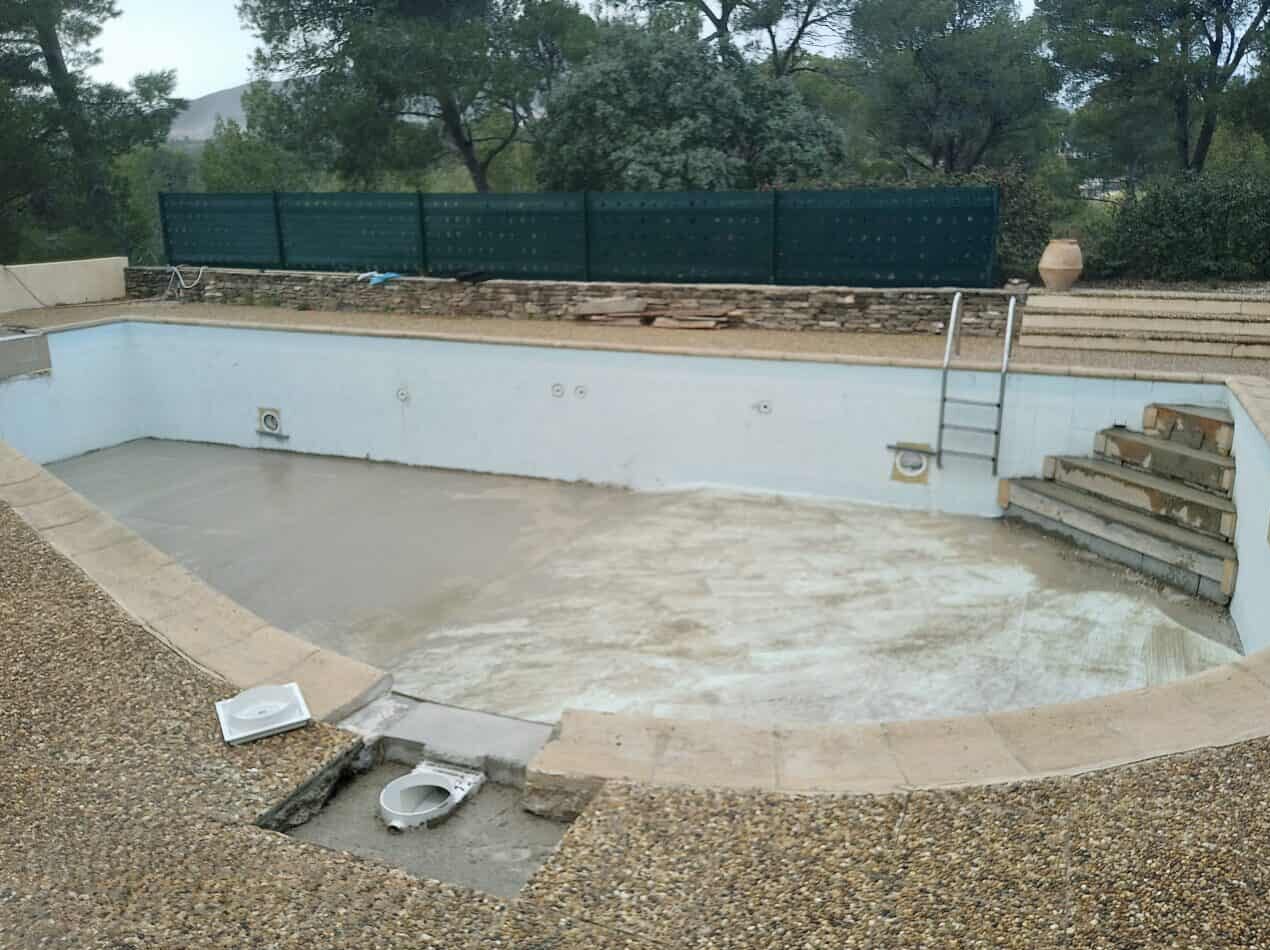 Piscine vide en rénovation avec escalier maçonné, margelles et bassin en béton sur un chantier extérieur.