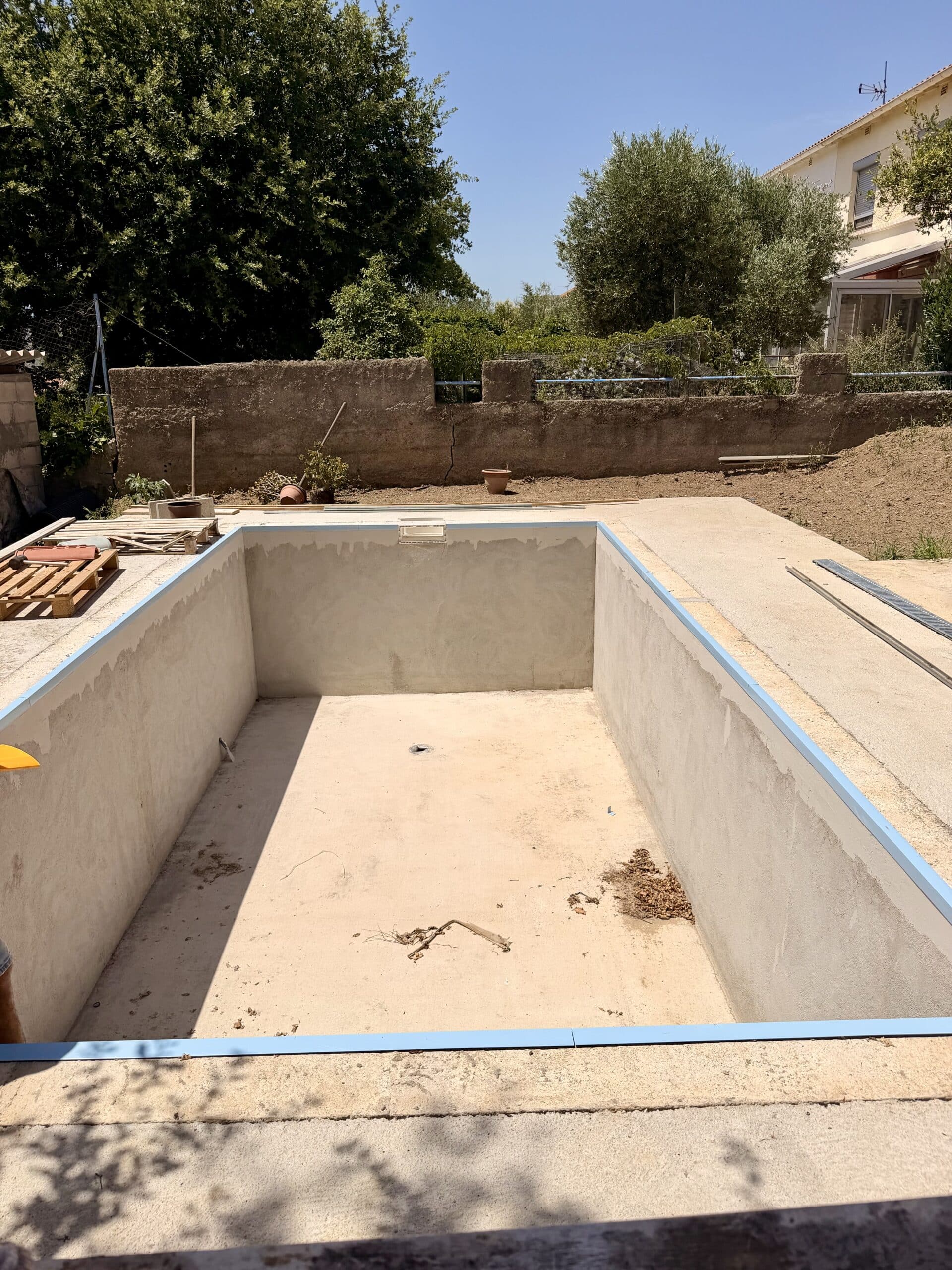 Construction d'une piscine creusée en béton avec rail bleu dans un jardin résidentiel.