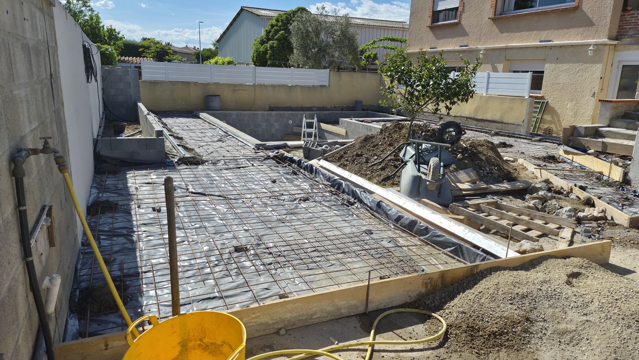 Chantier de construction d'une piscine avec treillis soudé et coffrage pour terrasse en béton.