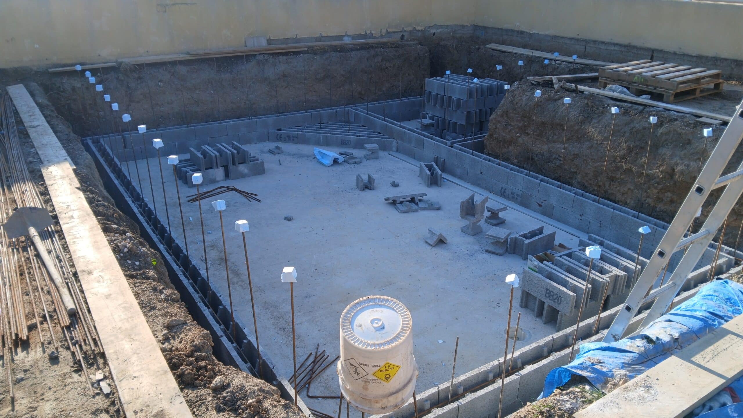 Chantier de piscine avec murs en blocs de béton, fers à béton sécurisés et matériel de construction en fond de fouille.