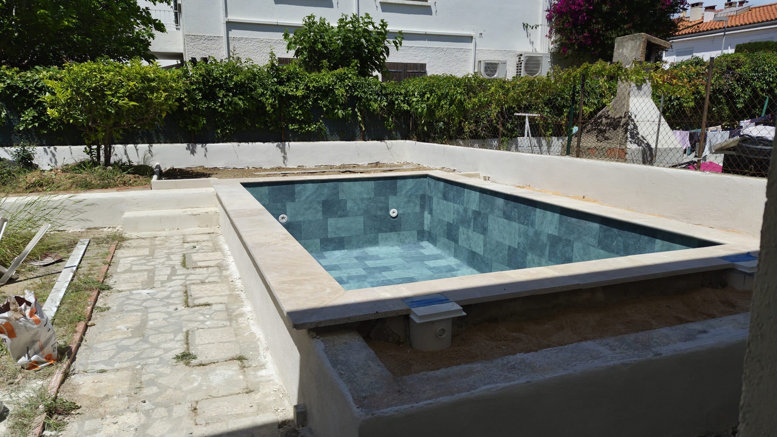 Petite piscine rectangulaire en carrelage bleu canard en cours de construction dans un jardin avec terrasse en pierre.