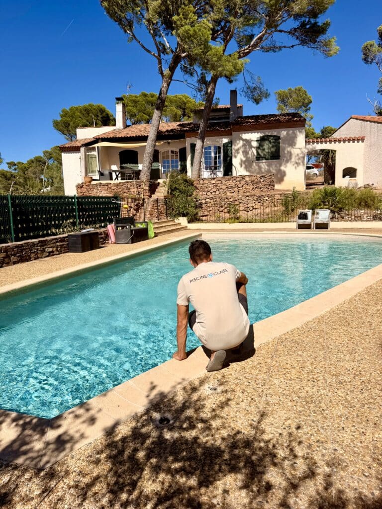 Piscine Claire : Service professionnel d'entretien de piscine Technicien Piscine Claire vérifiant l'eau d'une piscine devant une villa provençale sous un grand soleil.