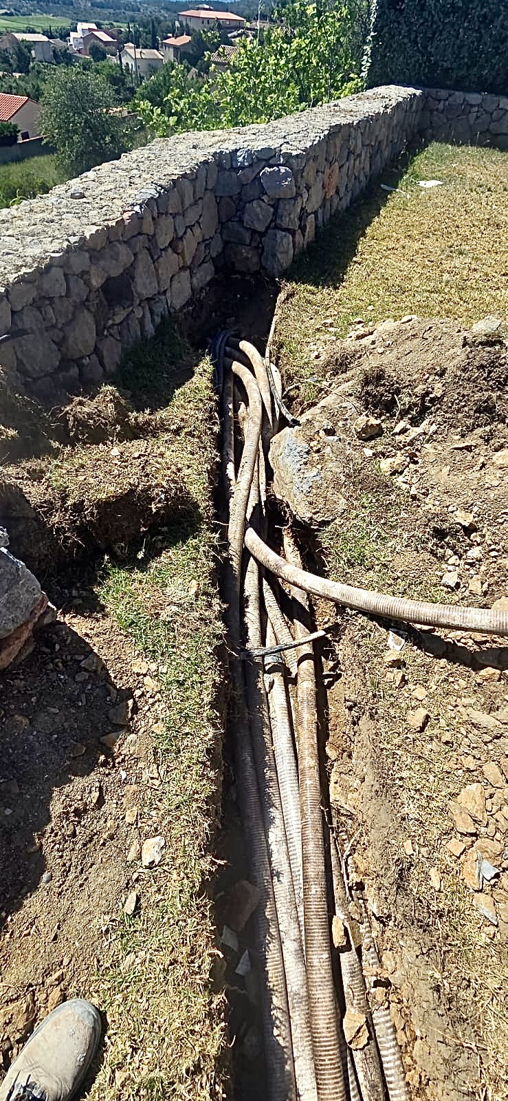 Plusieurs gaines annelées dans une tranchée le long d'un mur en pierres pour l'installation de réseaux extérieurs.