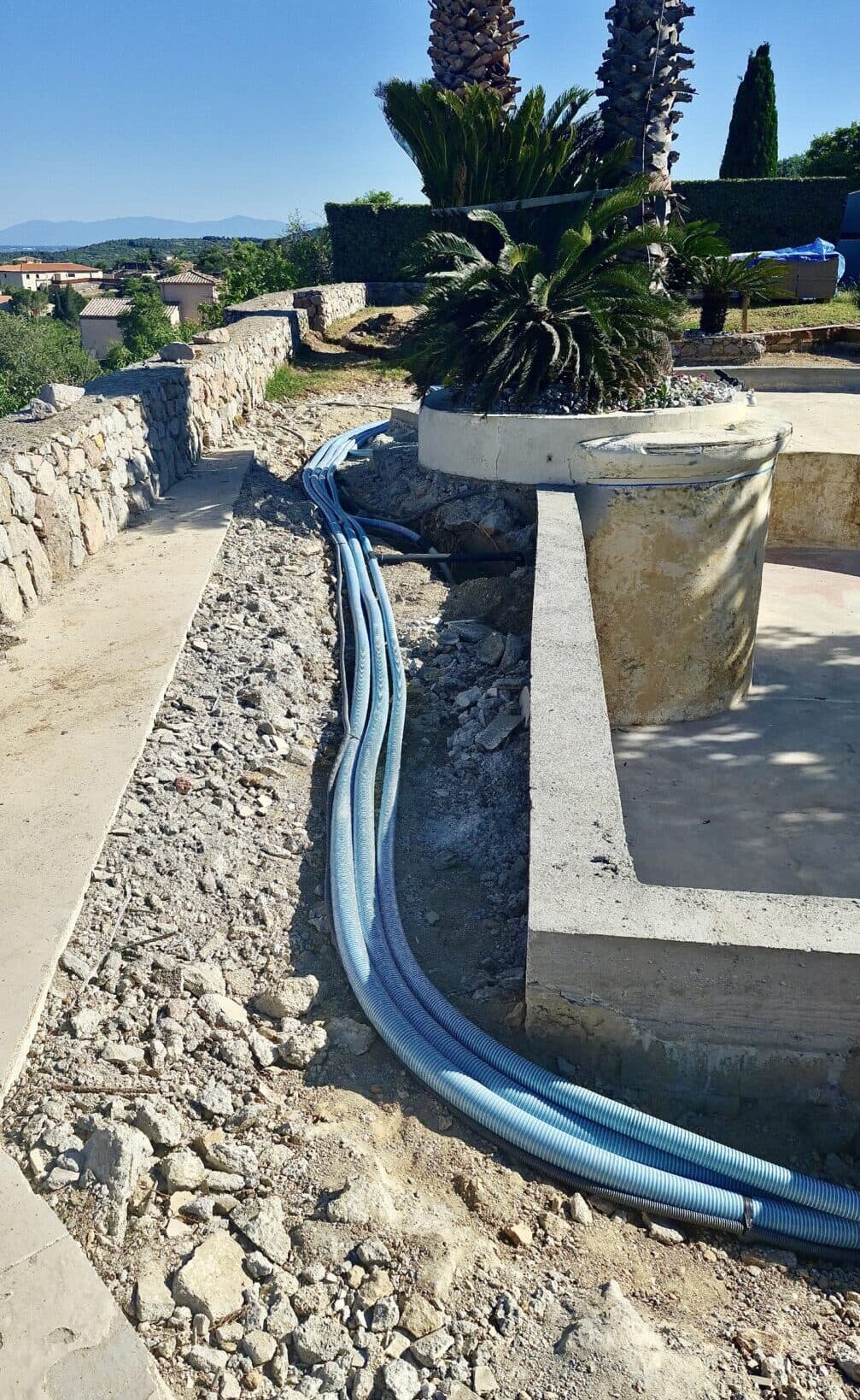 Gaines bleues flexibles pour piscine posées dans une tranchée de gravier lors de travaux d'aménagement extérieur.