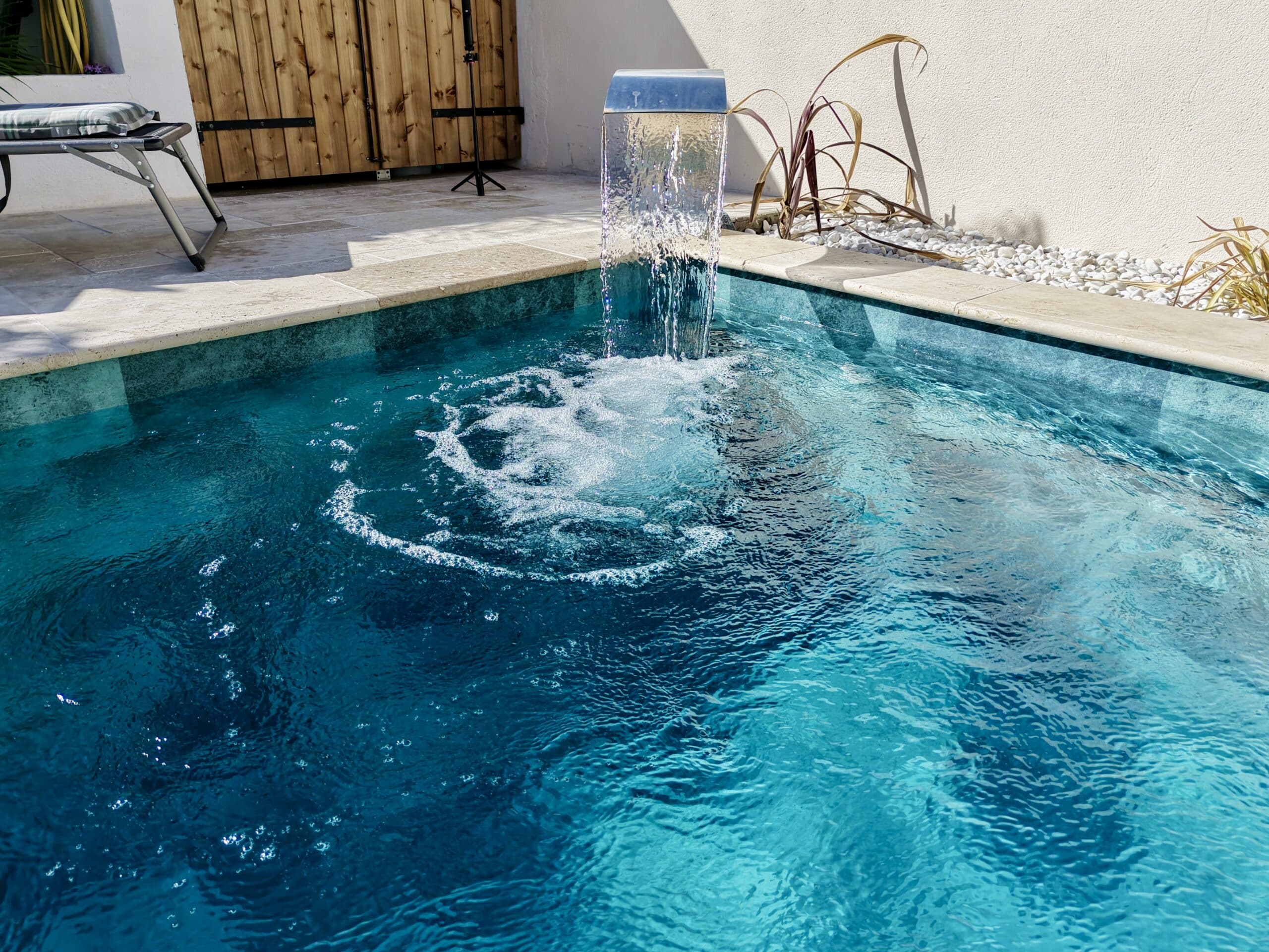 Cascade d'eau moderne se déversant dans une piscine bleue aux eaux cristallines sur une terrasse ensoleillée.