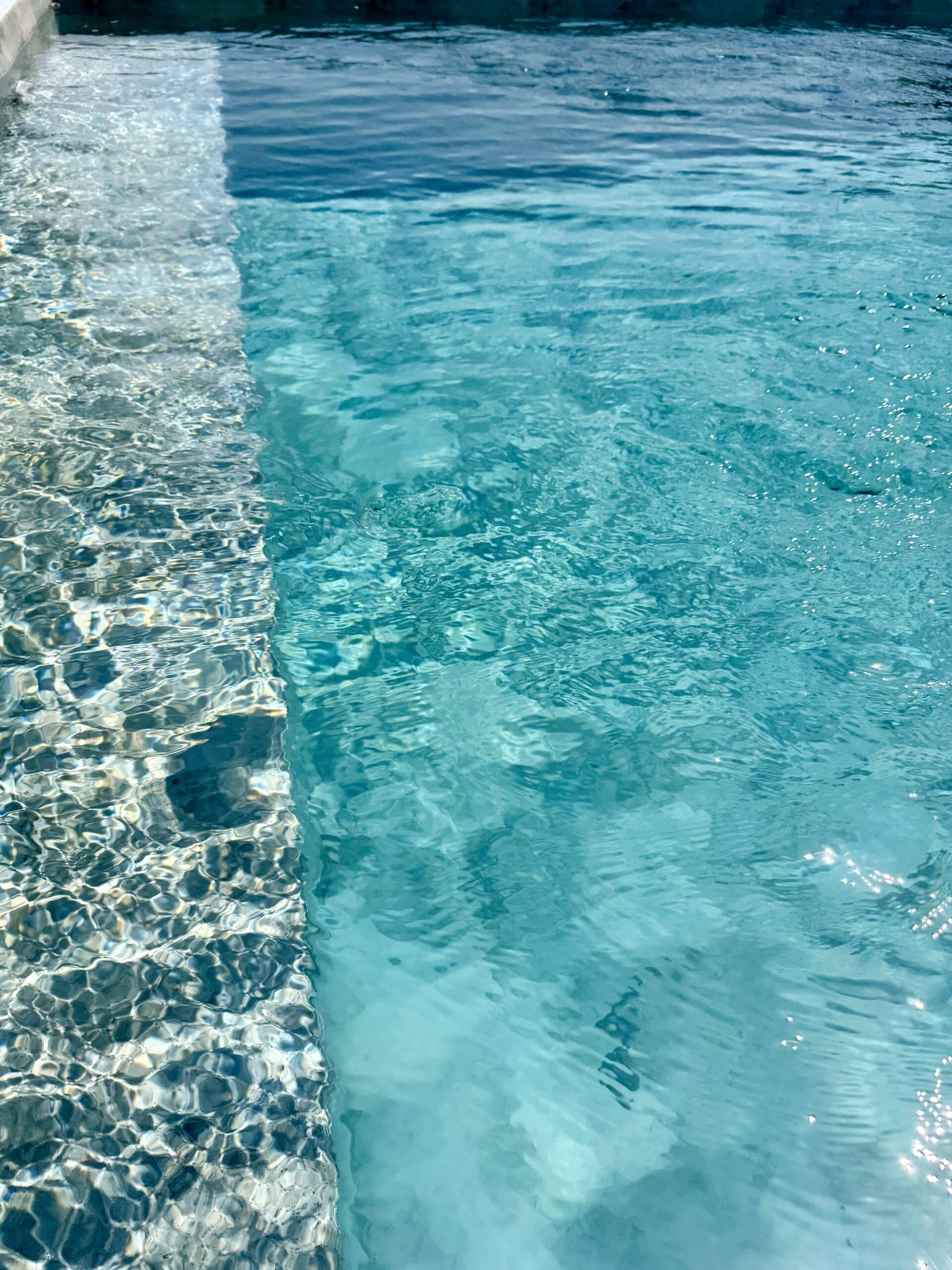 Eau de piscine turquoise scintillante avec reflets du soleil sur des marches immergées en mosaïque.