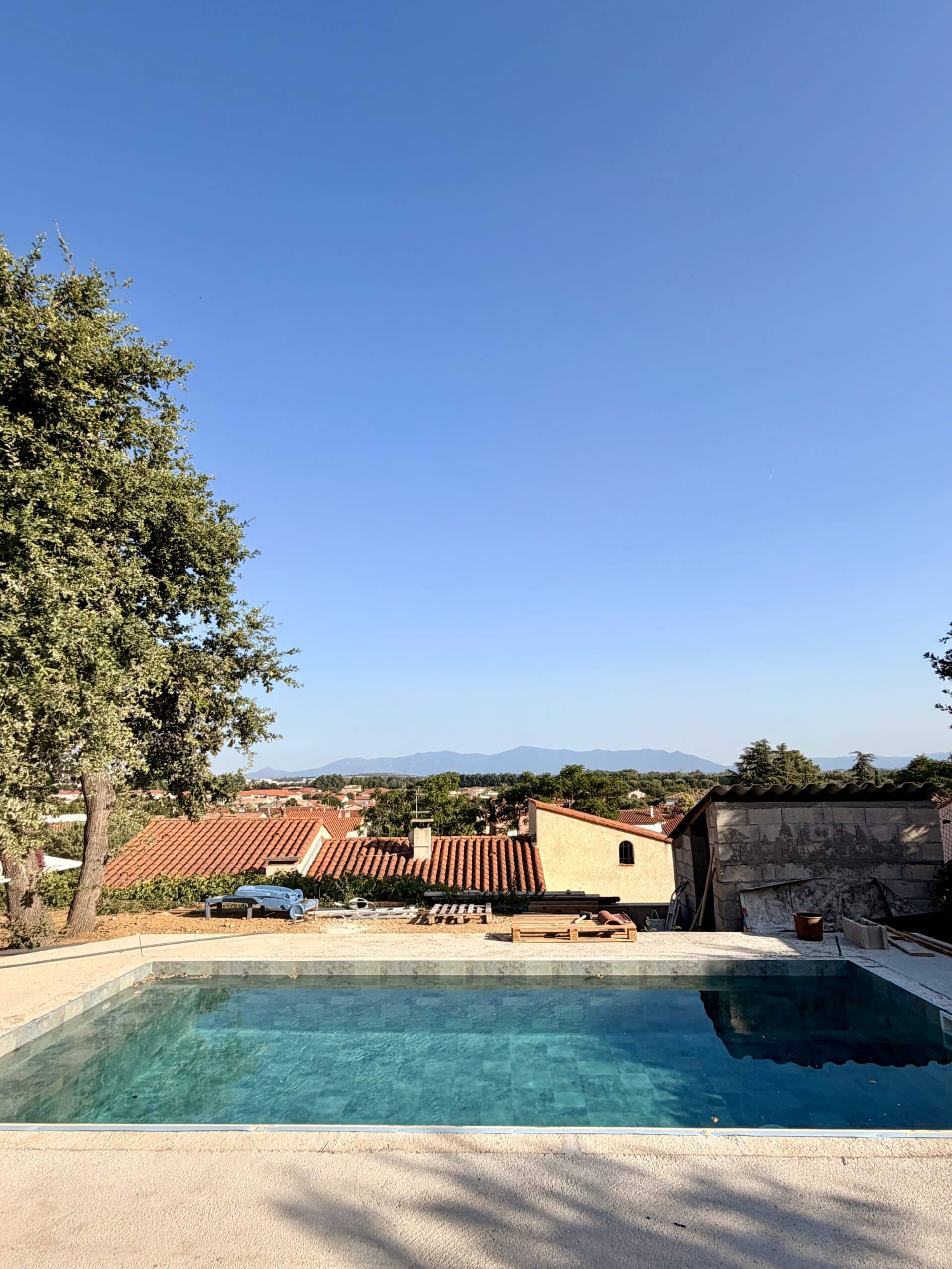 Piscine carrelée turquoise avec vue panoramique sur des toits en tuiles et des montagnes lointaines.