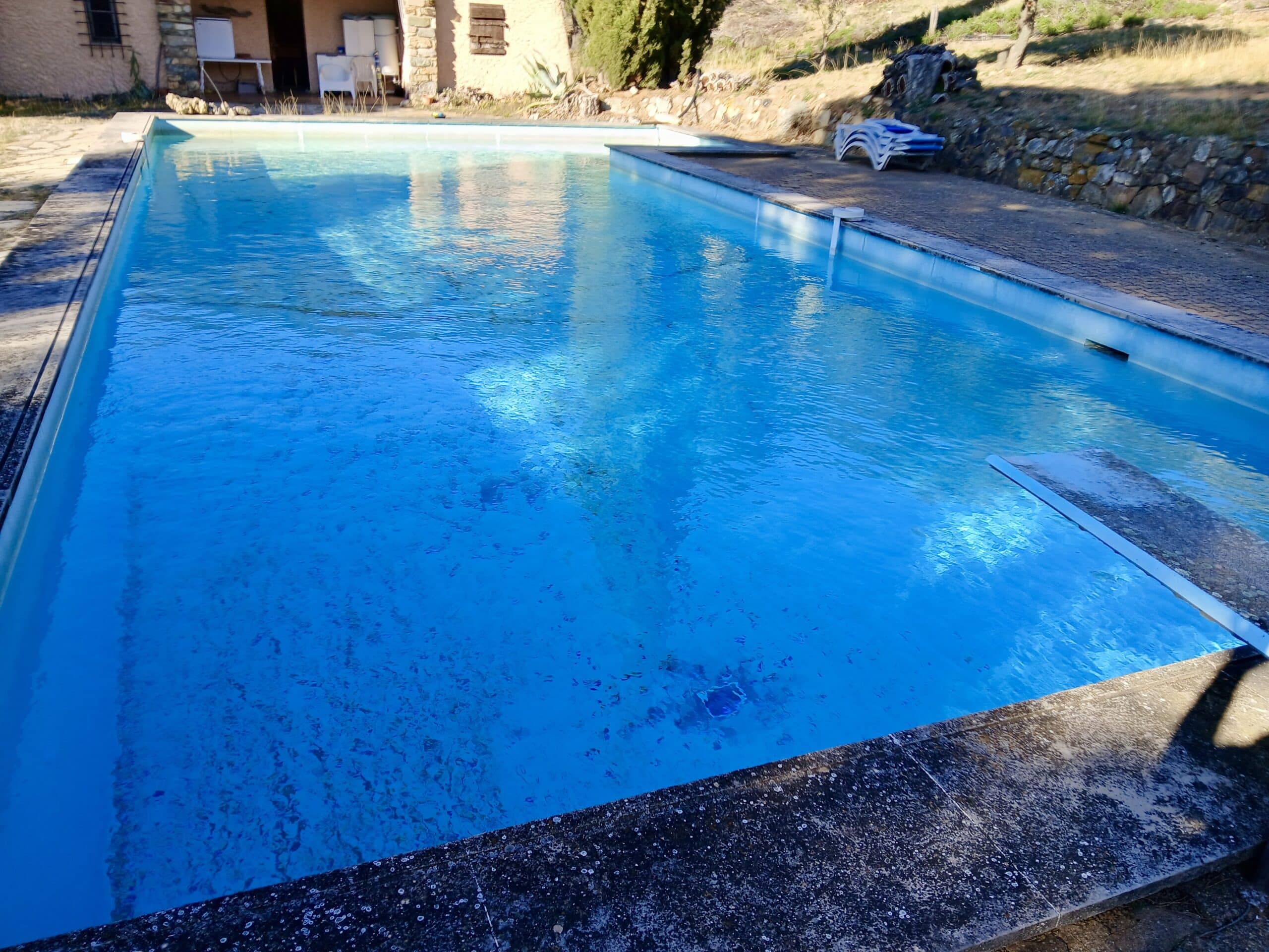 Piscine extérieure aux eaux bleues cristallines avec un plongeoir et une terrasse en pierre ensoleillée.