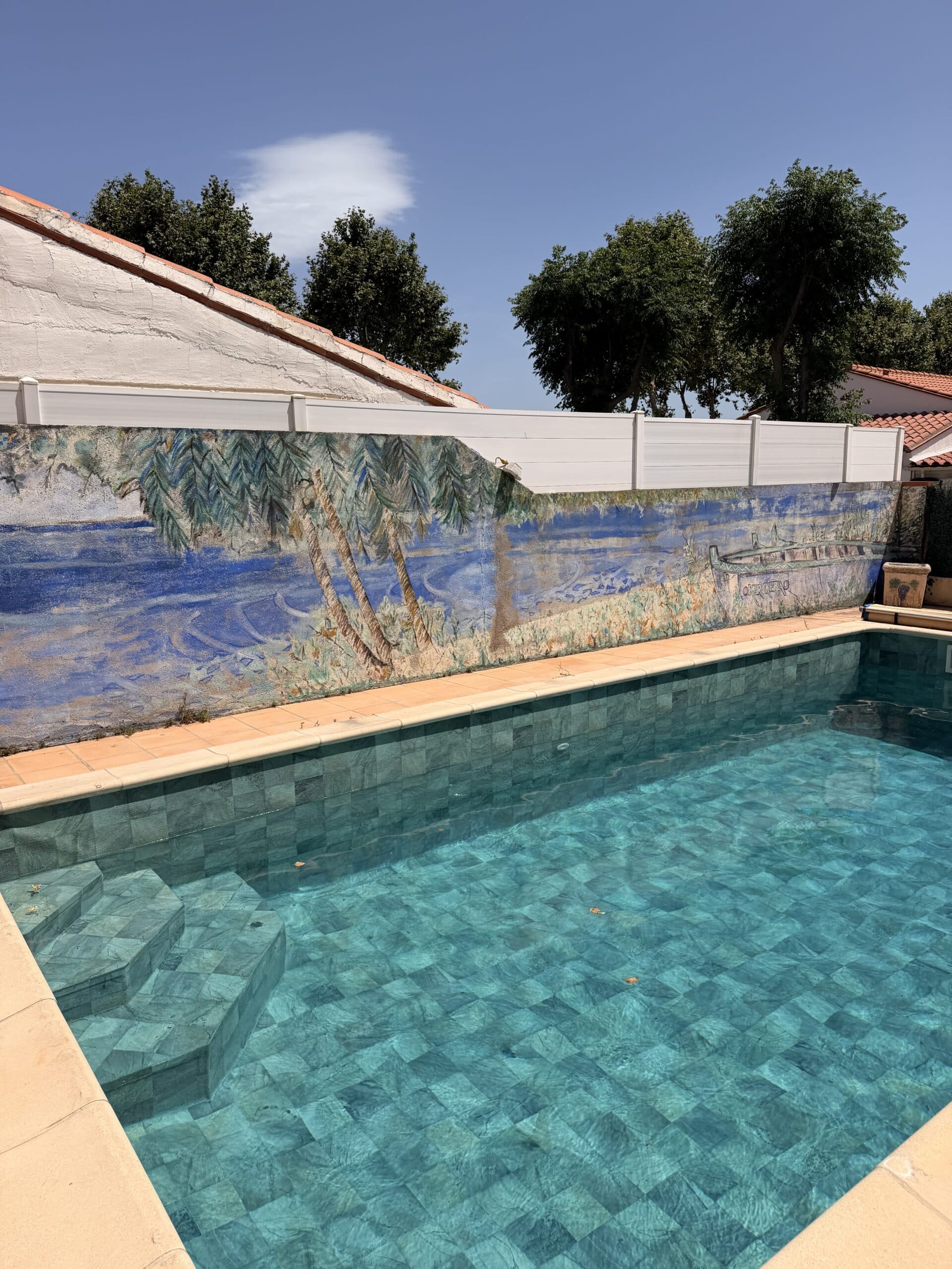 Piscine Mosaïque Turquoise et Fresque Murale Tropicale Piscine à mosaïque turquoise devant une fresque tropicale OKERBERO avec palmiers sous un ciel bleu.