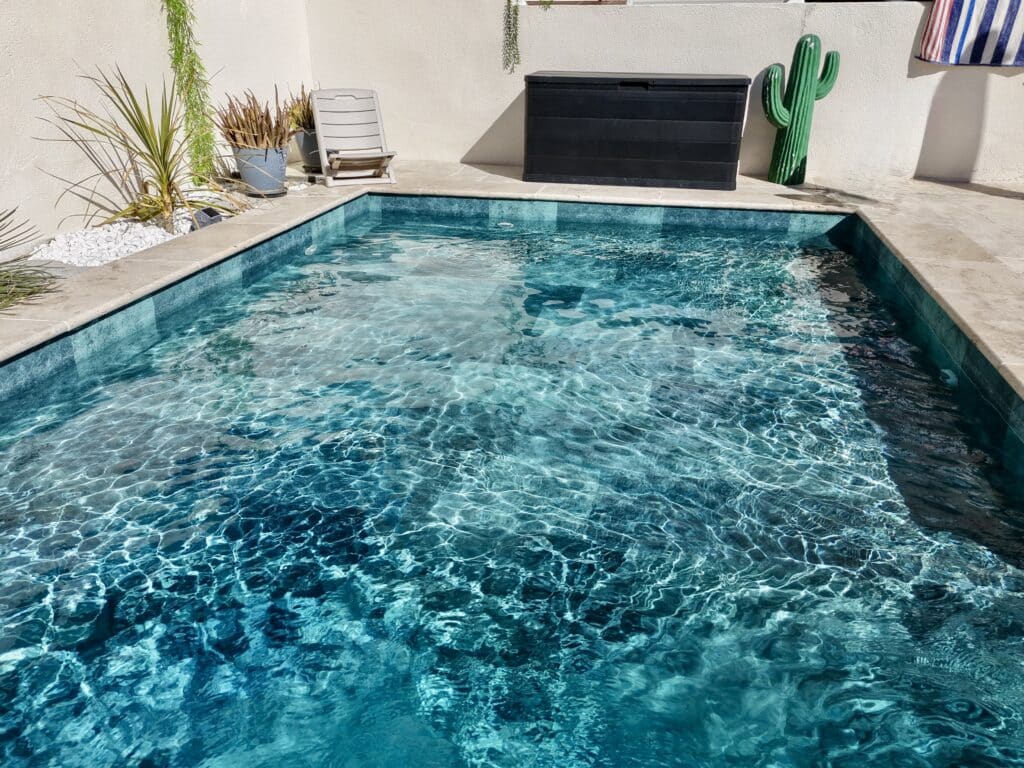 Piscine Turquoise Cristalline et Décoration de Jardin Piscine aux eaux turquoise cristallines entourée de dalles claires, plantes vertes et décor cactus original.