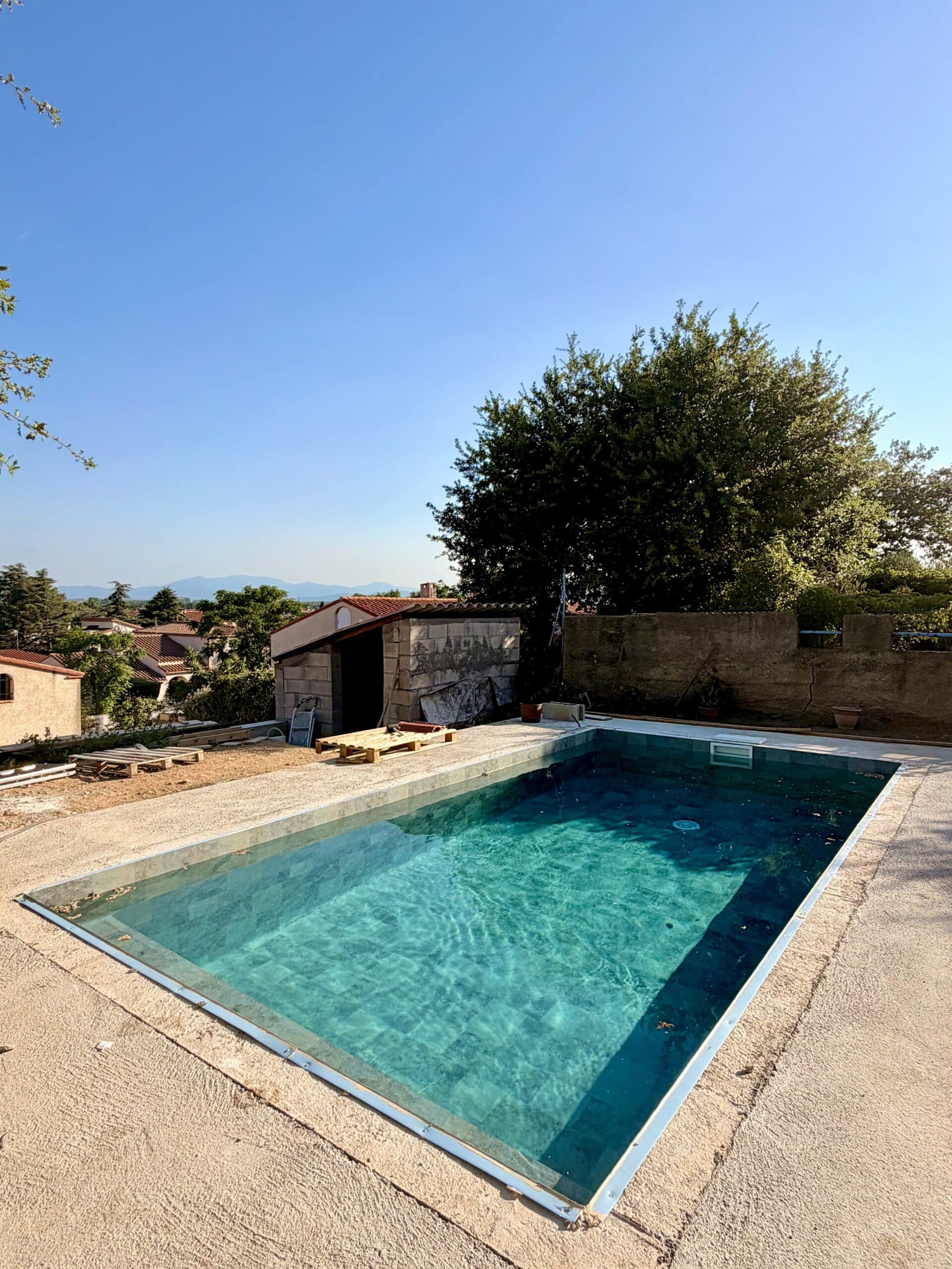 Piscine turquoise sur terrasse en béton avec vue panoramique sur les collines et un petit pool house en construction.