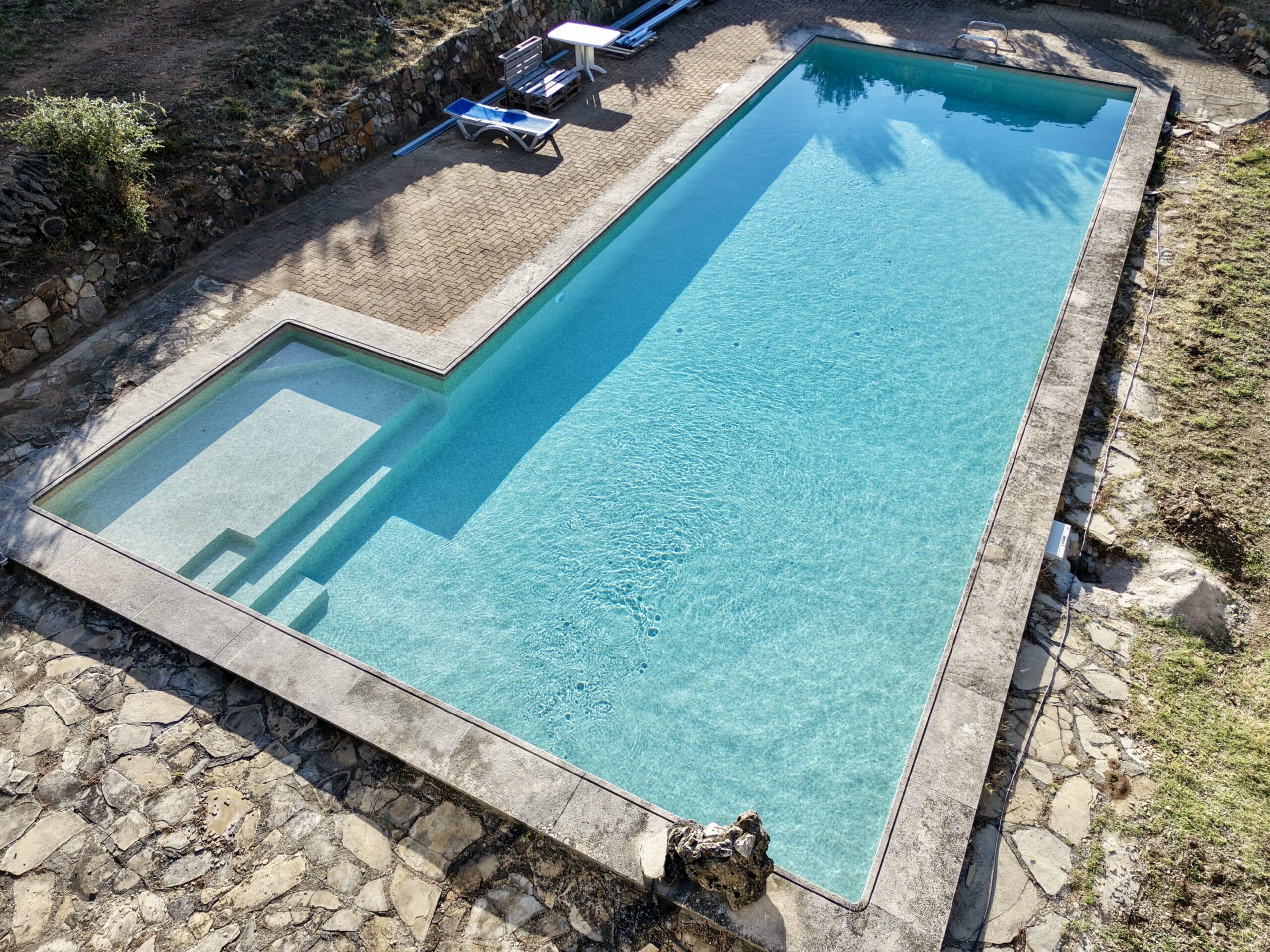 Grande piscine rectangulaire aux eaux turquoise avec escalier intégré sur une terrasse en pierre naturelle.