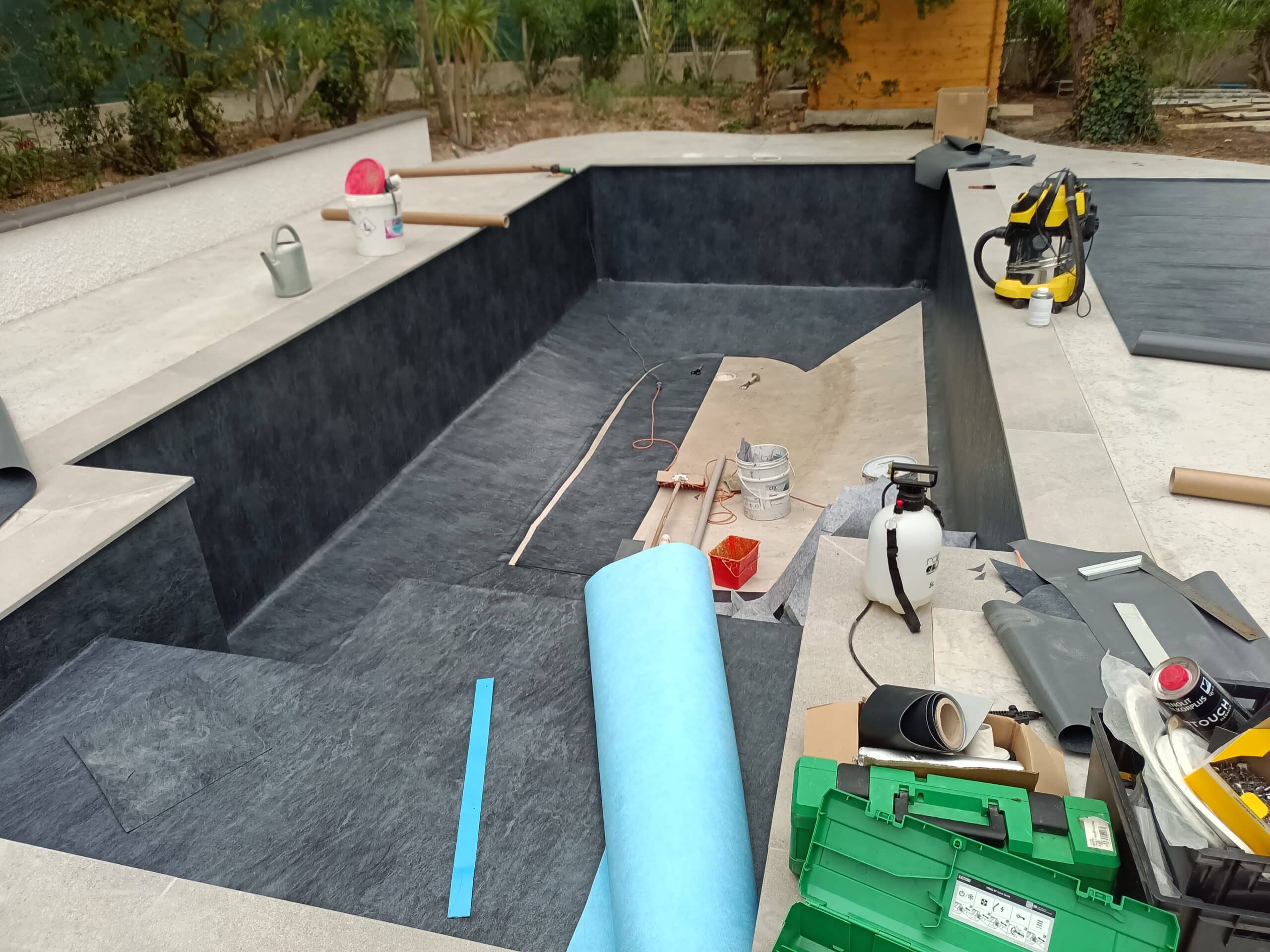 Chantier de rénovation de piscine avec pose d'une membrane armée gris ardoise et matériel de travaux.