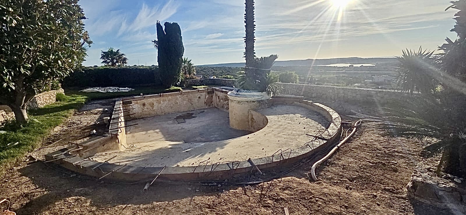 Chantier de rénovation d'une piscine en béton avec vue panoramique sur la mer sous un soleil éclatant.