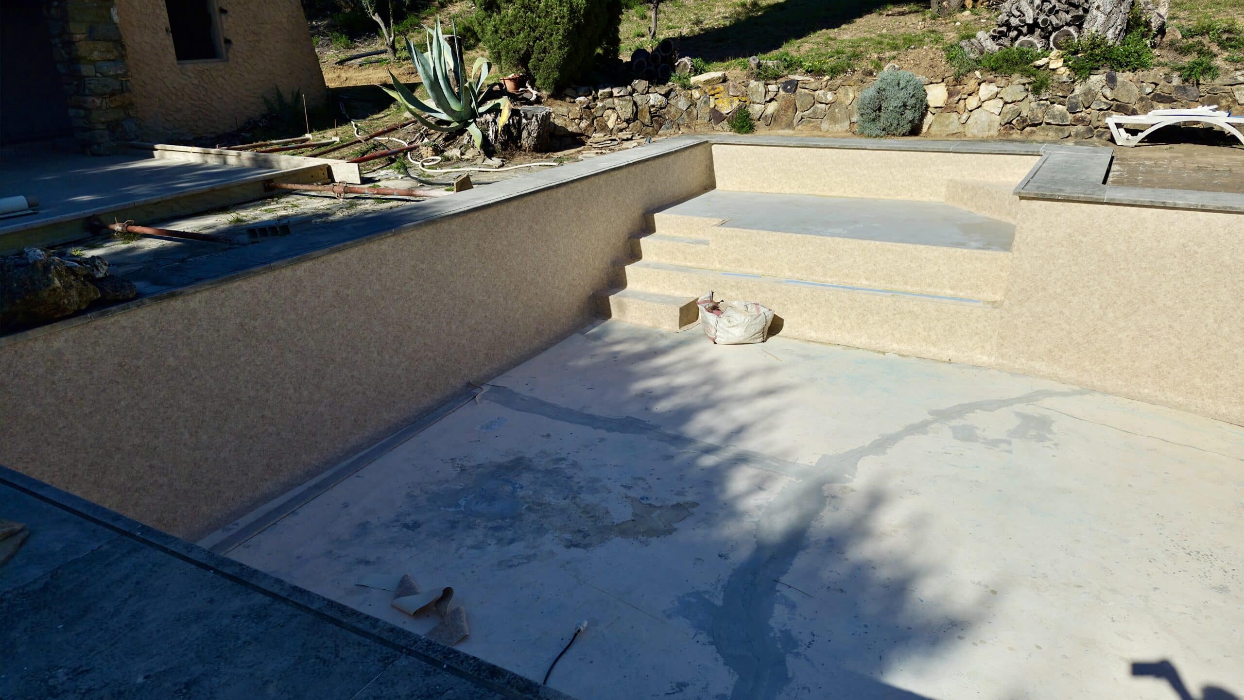 Piscine en rénovation avec liner beige, escalier intérieur et fond en béton en cours de travaux de finition.