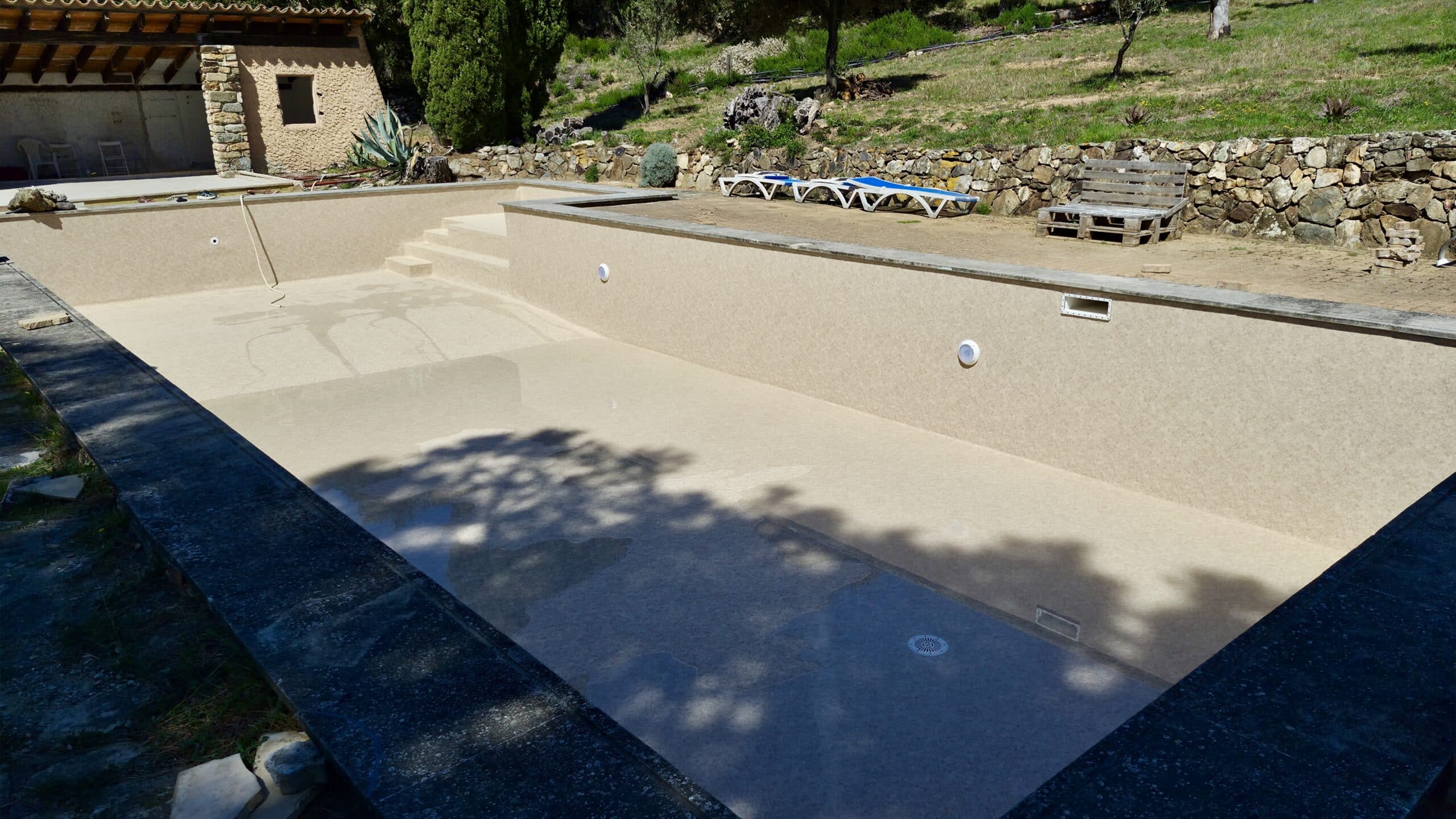 Piscine vide en rénovation avec liner couleur sable, escaliers et margelles en pierre dans un jardin ensoleillé.