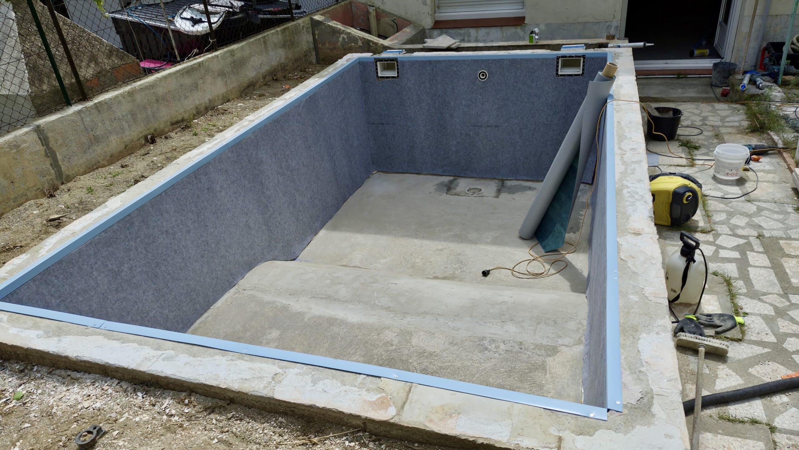 Chantier de rénovation de piscine avec pose de feutre de protection gris sur parois et préparation du liner.