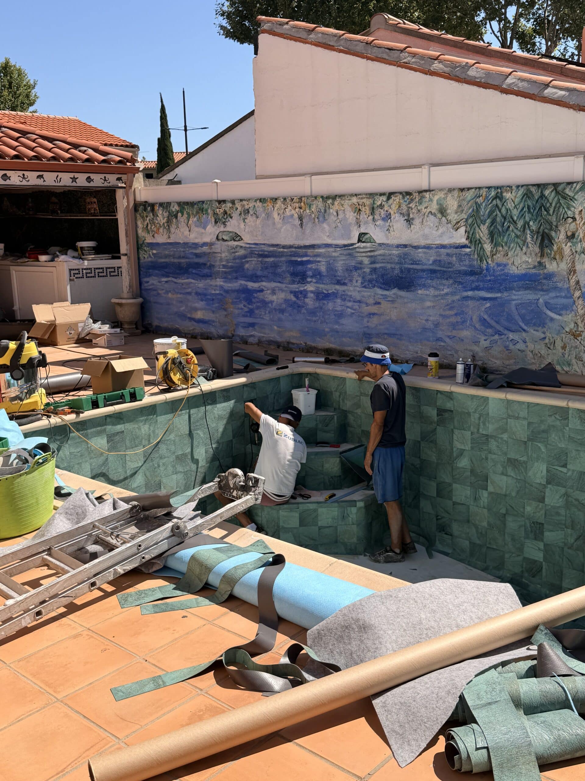 Rénovation de piscine : pose de liner PVC armé Zodiac par des ouvriers sur escalier et carrelage vert.