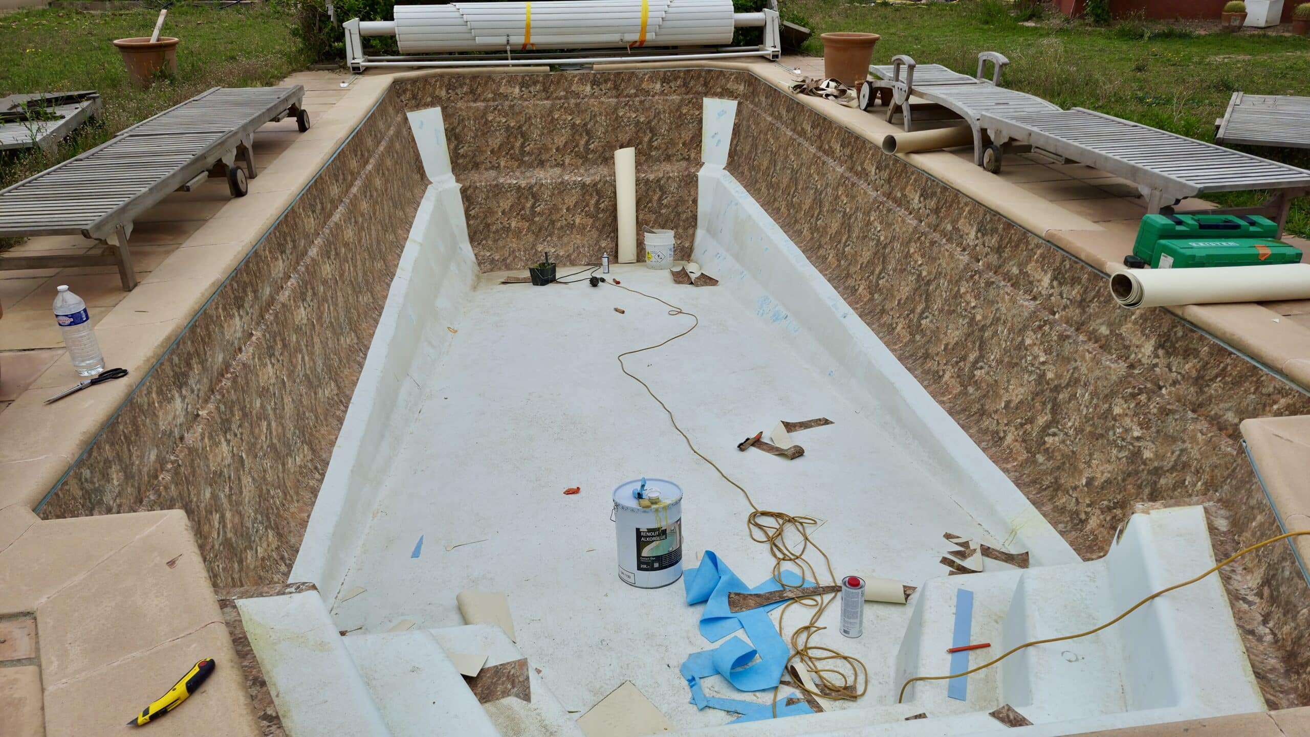 Chantier de rénovation d'une piscine : pose d'un liner à motif marbré avec outils et pot de colle Renolit Alkorplan.