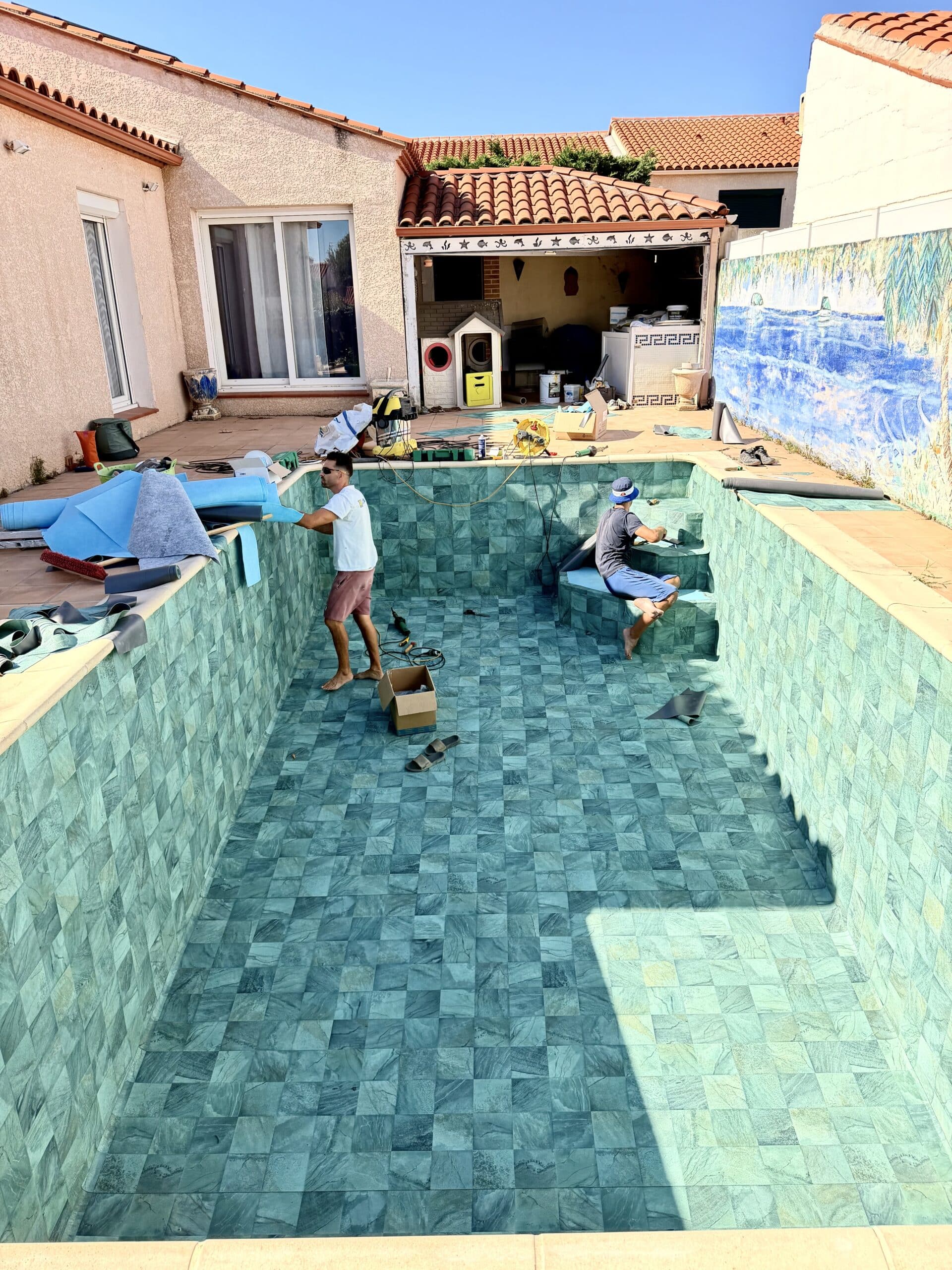 Ouvriers en pleine rénovation d'une piscine vide au revêtement aspect pierre verte avec pose de liner.