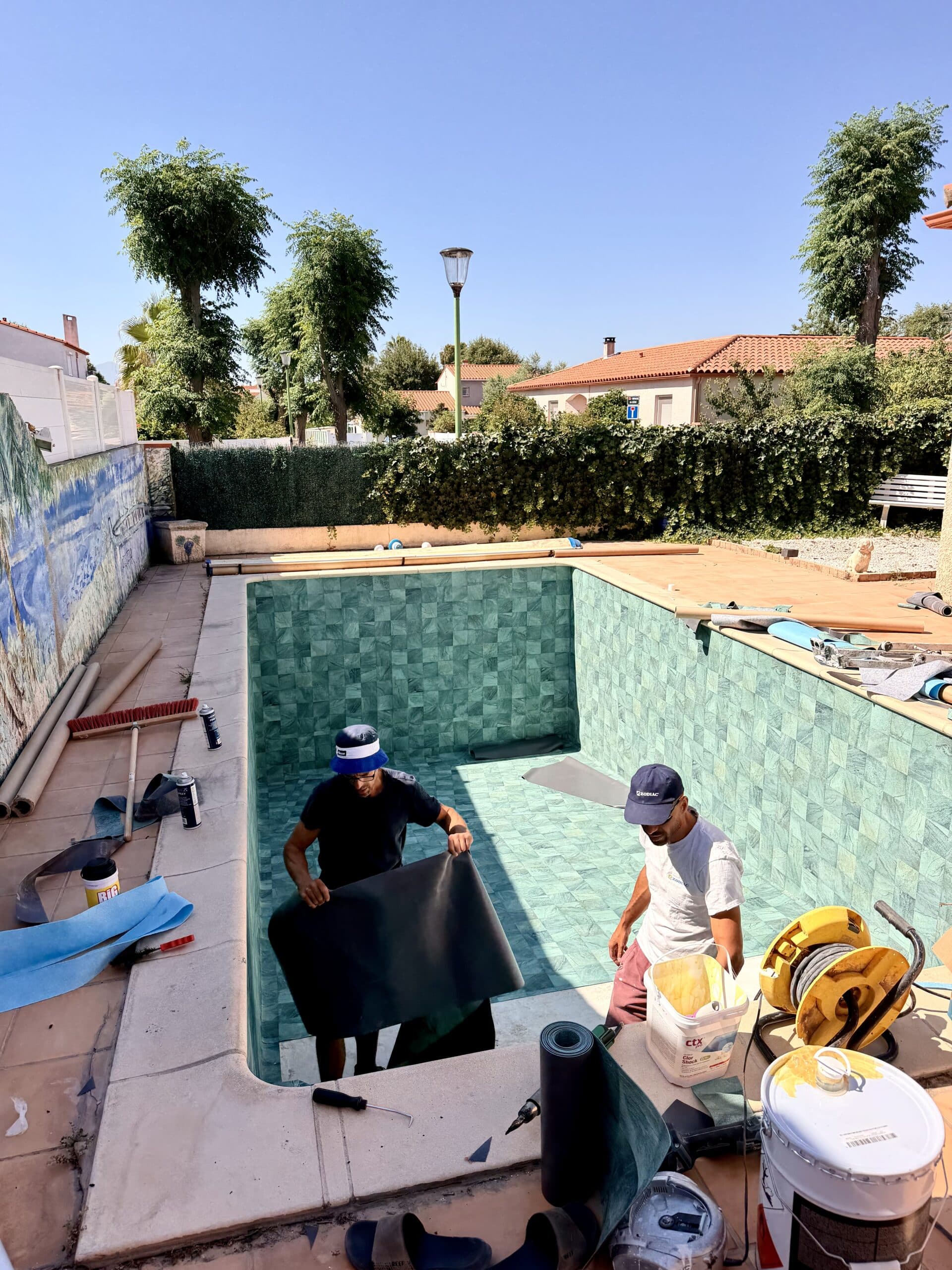 Artisans installant un liner de piscine. Seau ctx Clor Shock et matériel Zodiac visibles lors de la rénovation.