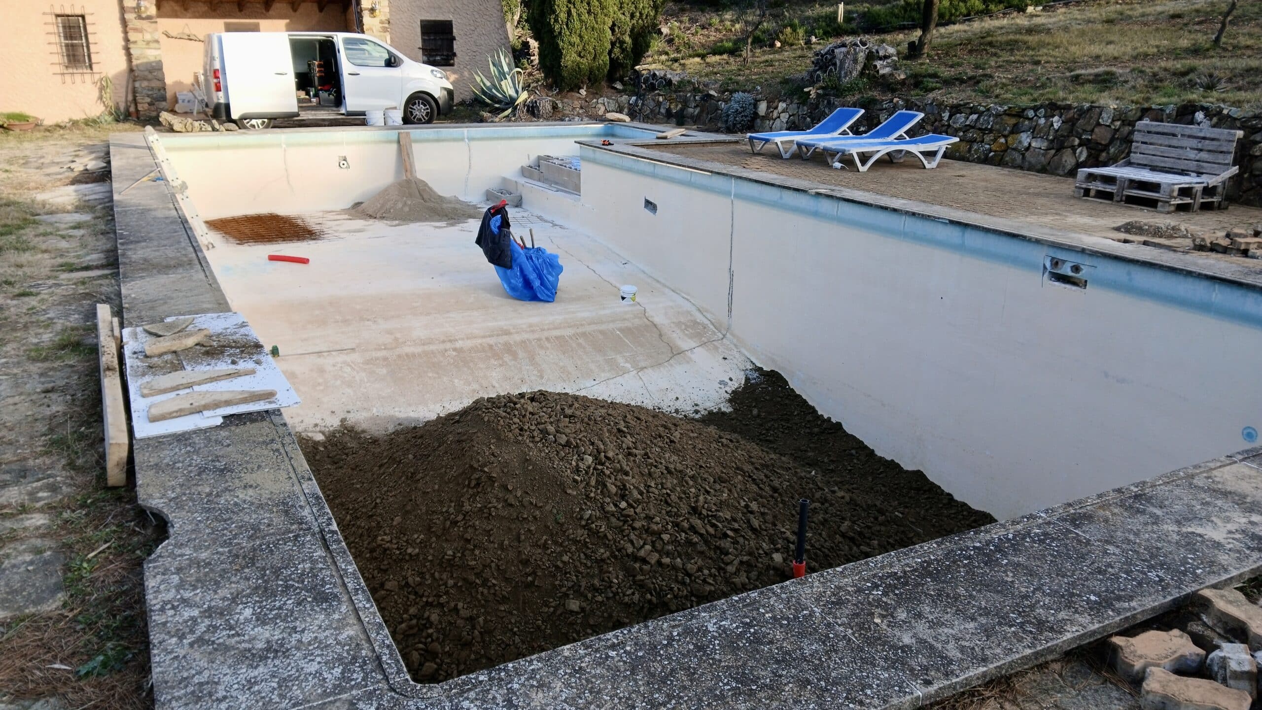 Rénovation de piscine : bassin vidé et partiellement rempli de terre avec matériaux de construction et camionnette.