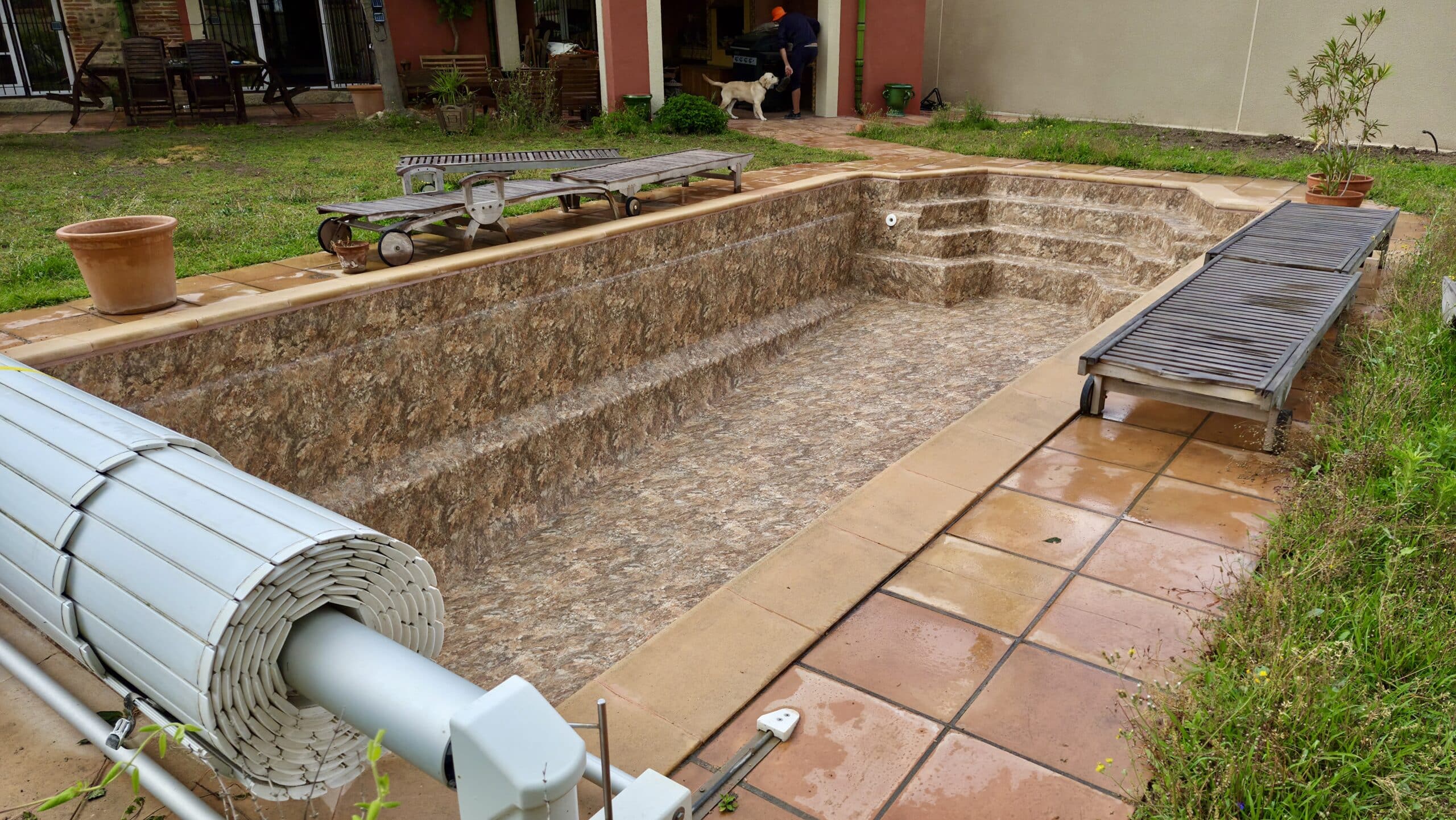 Piscine vide rénovée avec liner aspect pierre, volet roulant et transats sur une terrasse en dalles.